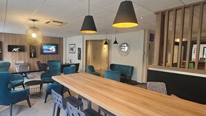 A modern interior with teal chairs, a wooden table, pendant lighting, and a TV screen. - Hôtel des Halles (Dijon)