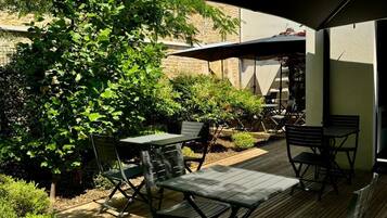 Un patio al aire libre con suelo de madera, sillas y mesas de metal bajo un gran paraguas.