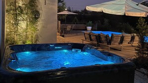 A hot tub with a blue light, surrounded by outdoor furniture and umbrellas.