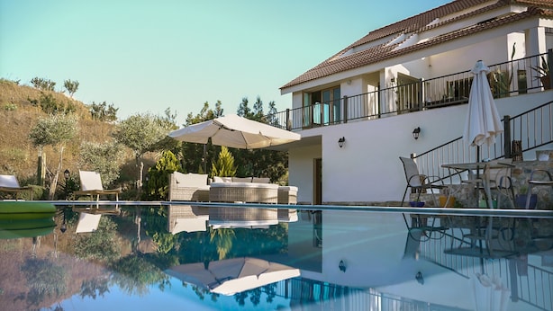 A poolside area with a clear pool, outdoor furniture, and a two-story building with balconies.