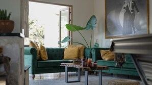A green sofa with yellow cushions, a marble coffee table, and a large plant.