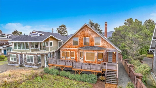 Une maison en bois à deux étages, dotée d’un balcon et d’une terrasse, entourée d’un jardin aménagé.