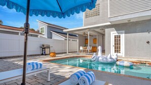 A backyard with a swimming pool, lounge chairs, and a barbecue area.