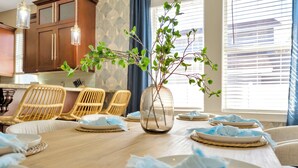 A dining area with a wooden table set for a meal, surrounded by wicker chairs, and a vase with branches on the table.