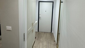 En smal hall med trägolv, vita väggar och en dörr längst in.