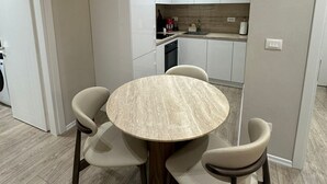 Ett modernt kök med vita skåp, ett runt matbord med fyra stolar och en inbyggd ugn.