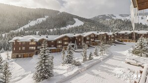 A snow-covered lodge with multiple buildings, a ski slope in the background, and a clear sky. - 2BR Ski-In/Ski-Out Condo, Private & Quiet, Steps to Lone Moose Lift – Big Sky (Big Sky)