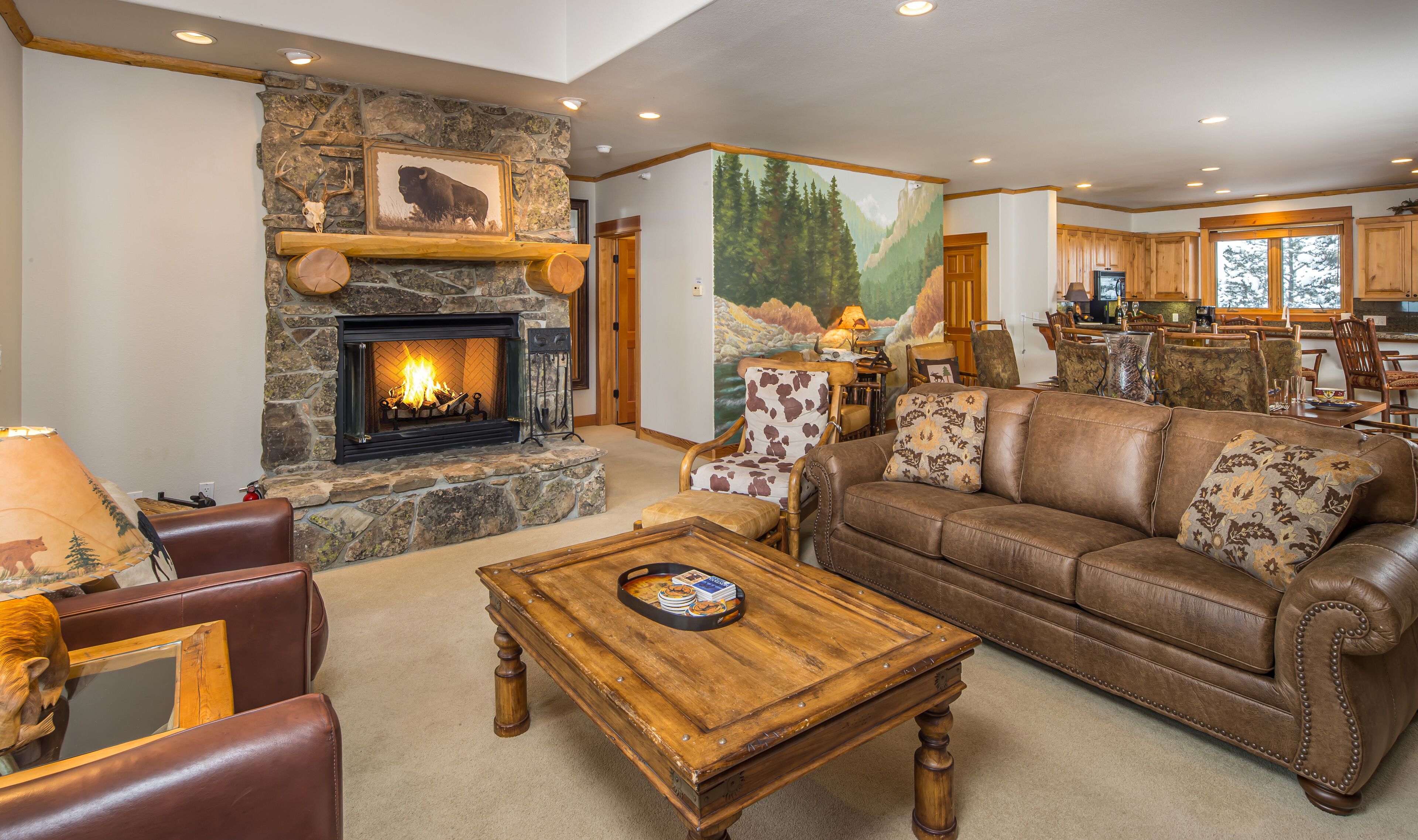 A cozy living room with a stone fireplace, leather furniture, and a mural of a forest scene.