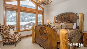 A bedroom with a large wooden bed, a wooden armchair, and a view of snowy mountains through large windows. - 2BR Ski-In/Ski-Out Condo, Private & Quiet, Steps to Lone Moose Lift – Big Sky (Big Sky)