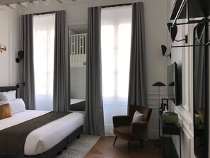 Une chambre d’hôtel avec un lit, une chaise, un bureau et une grande fenêtre avec des rideaux.