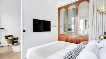 Een moderne slaapkamer met een groot bed, een houten garderobe met spiegels, een televisie aan de muur en een stoel.