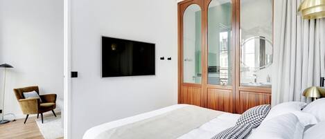 A modern bedroom with a large bed, a wooden wardrobe with mirrors, a television on the wall, and a chair.