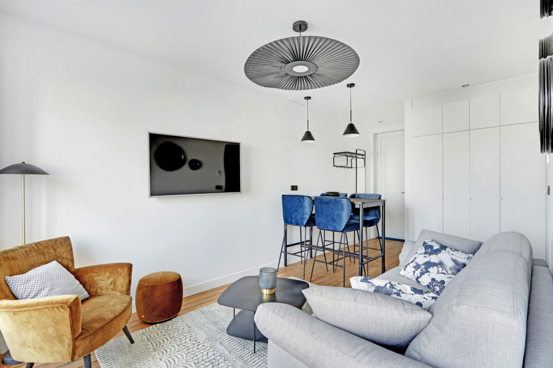 A modern living room with a grey sofa, a brown armchair, and a dining area with blue chairs.