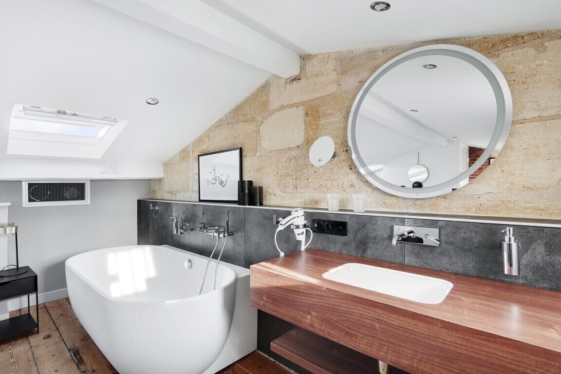 A modern bathroom with a freestanding bathtub, a wooden vanity, a large mirror, and a stone accent wall.