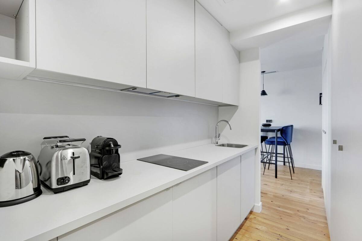 A modern kitchen with white cabinets, a countertop, a kettle, a toaster, and a coffee maker.