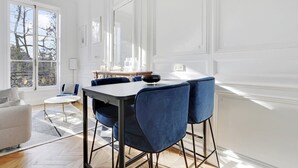 A modern dining area with a white table and blue chairs, large windows, and a view of trees outside. - Maison Labruyère (Bordeaux)