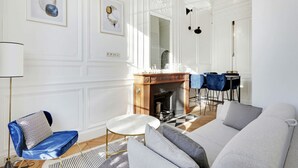 A spacious living room with a fireplace, a dining area with blue chairs, and a large mirror. - Maison Labruyère (Bordeaux)
