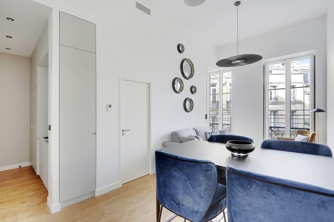 Una cocina moderna con armarios blancos, una mesa de comedor con sillas azules y un ventanal con vistas a edificios.