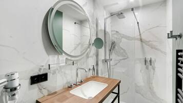 A modern bathroom with a marble shower, a wooden vanity, and a round mirror.
