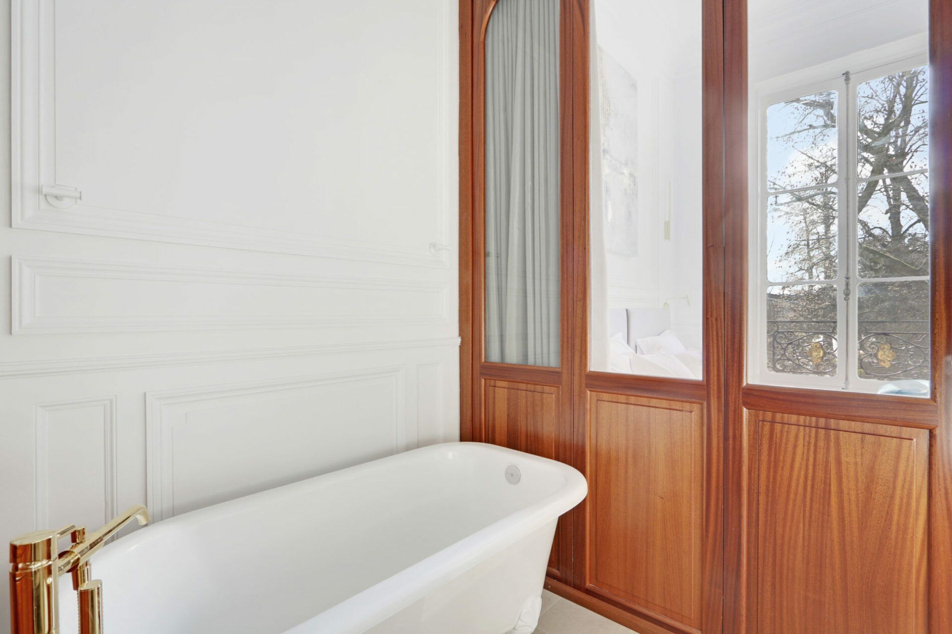 Une salle de bain avec une baignoire sur pieds, un lambris en bois et une fenêtre donnant sur la forêt.