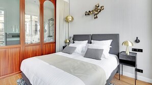 A modern bedroom with a large bed, wooden wardrobe, and a decorative wall piece. - Maison Labruyère (Bordeaux)