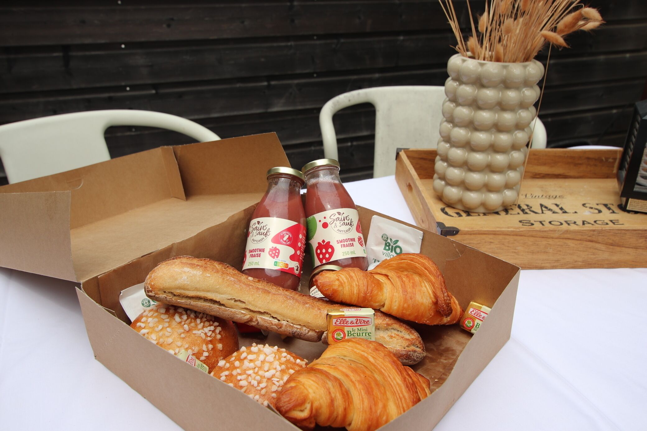 Eine Schachtel mit verschiedenen Lebensmitteln, darunter Croissants, eine Baguette und Saftflaschen.
