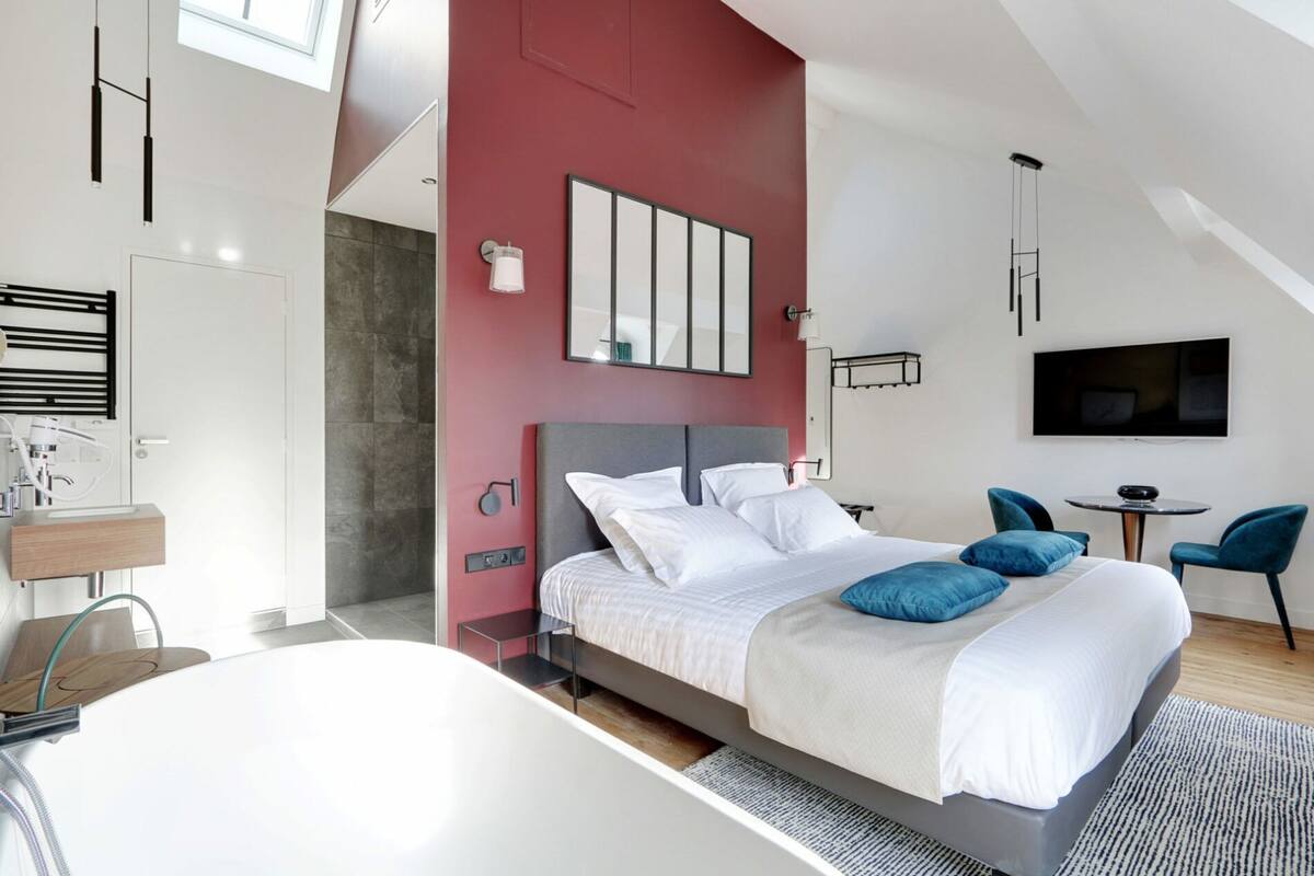 A modern hotel room with a large bed, a desk with a chair, a TV, and a balcony.