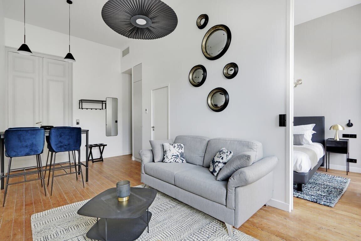 A modern living room with a grey sofa, two blue chairs, a coffee table, and a dining area with a white table and chairs.