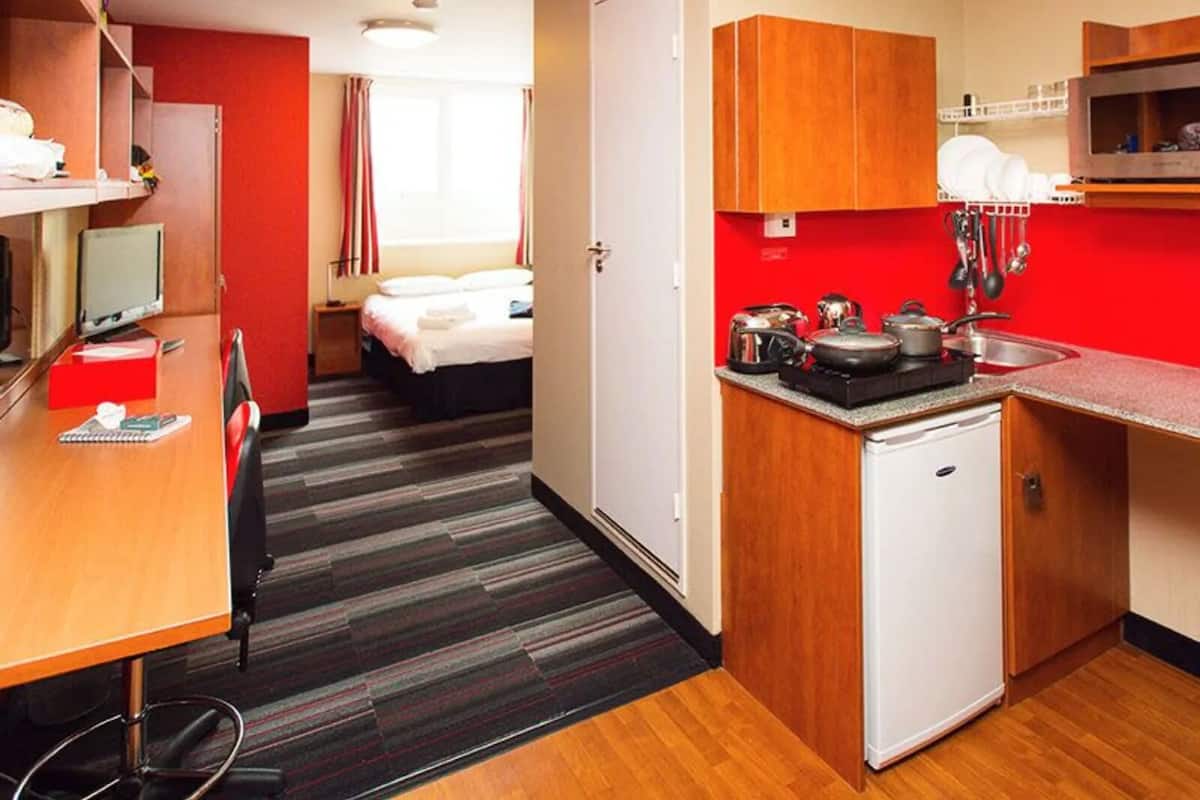 A hotel room with a bed, a desk with a computer, a small kitchenette, and a bathroom.