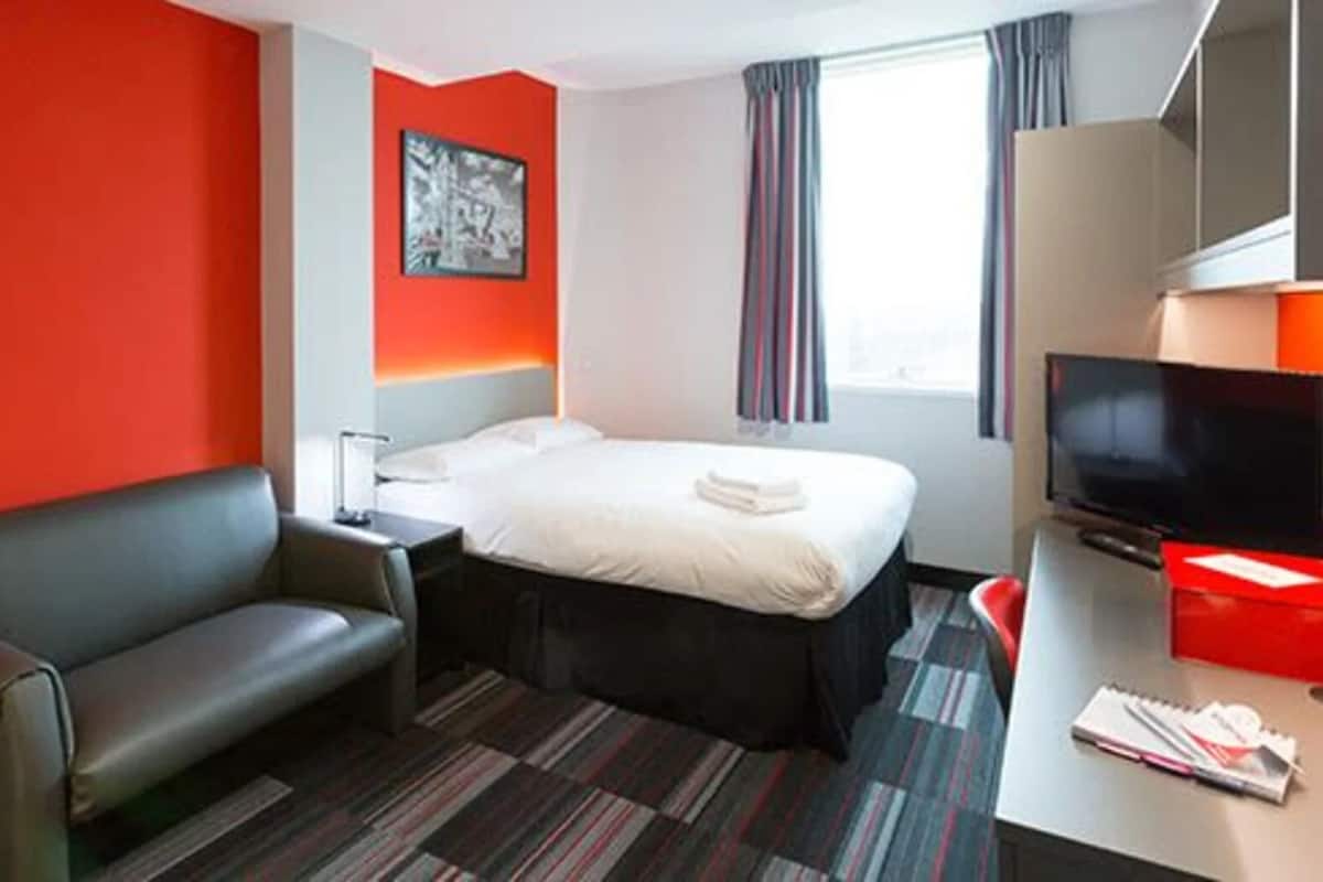 A hotel room with a bed, a desk, a TV, and a red wall.