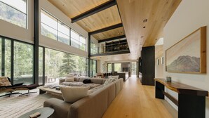 A spacious living area with a large sectional sofa, a coffee table, and a dining table. There are large windows providing natural light and views of the outdoors.