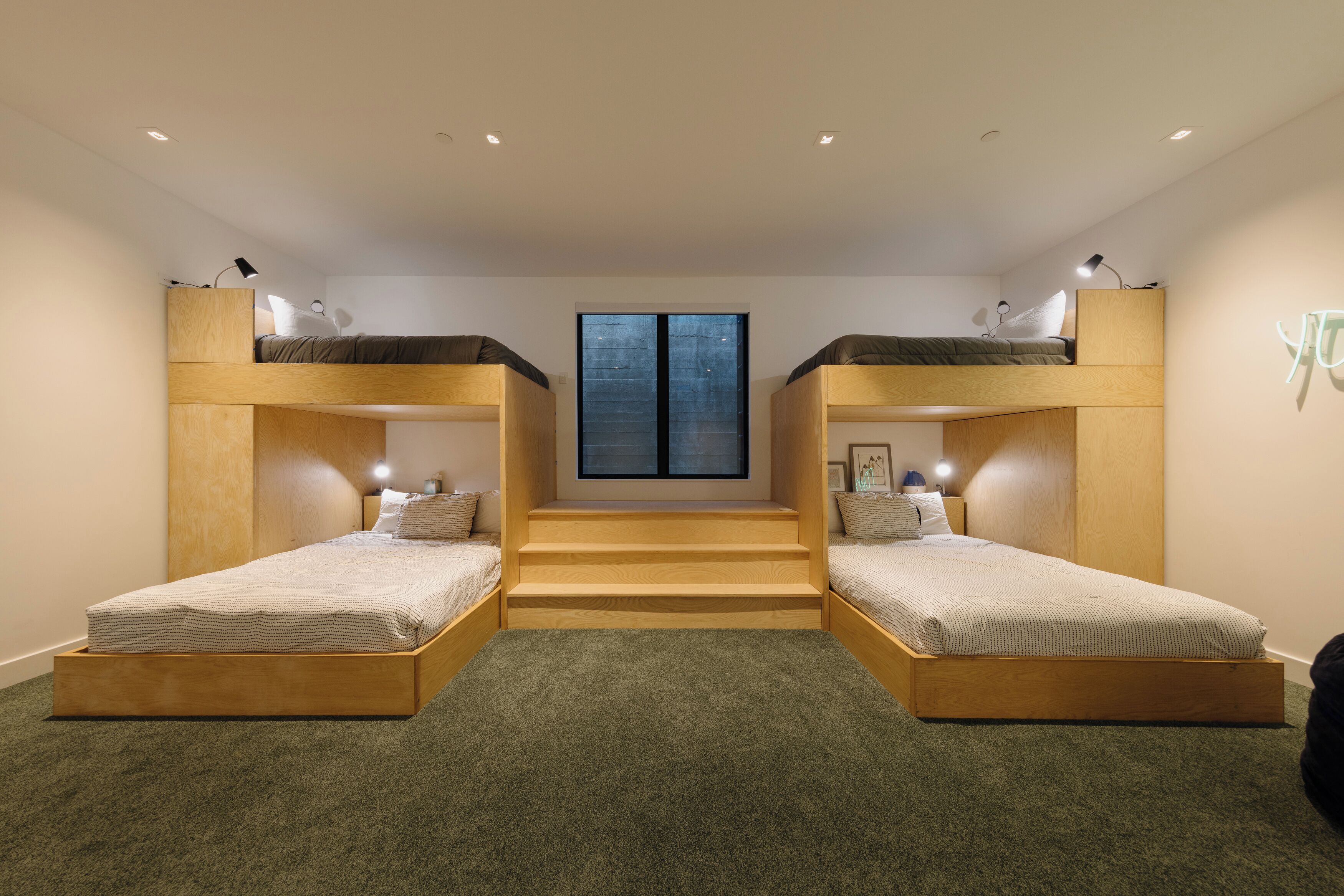 A room with two bunk beds, a staircase, and a large window.