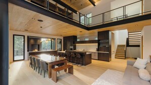 A modern kitchen with a central island, a dining area with a wooden table and chairs, and a staircase leading to an upper level.