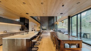 A modern kitchen with a central island, bar stools, and a long wooden table.