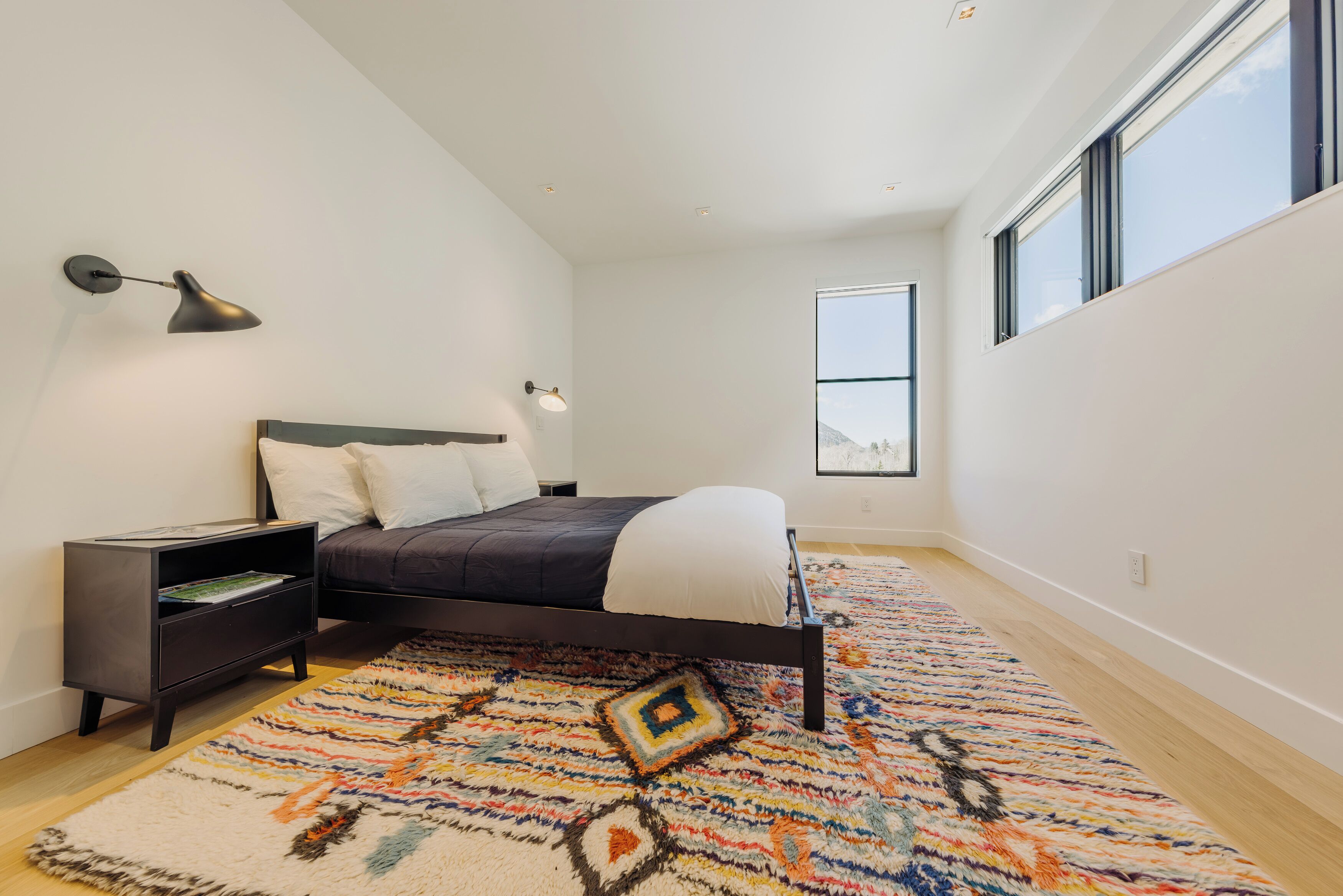 A bedroom with a bed, a nightstand, a lamp, a window, and a patterned rug.