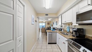 A modern kitchen with white cabinetry, a stainless steel dishwasher, a built-in oven, and a microwave. - Ocean House 1403 by Liquid Life (Gulf Shores)
