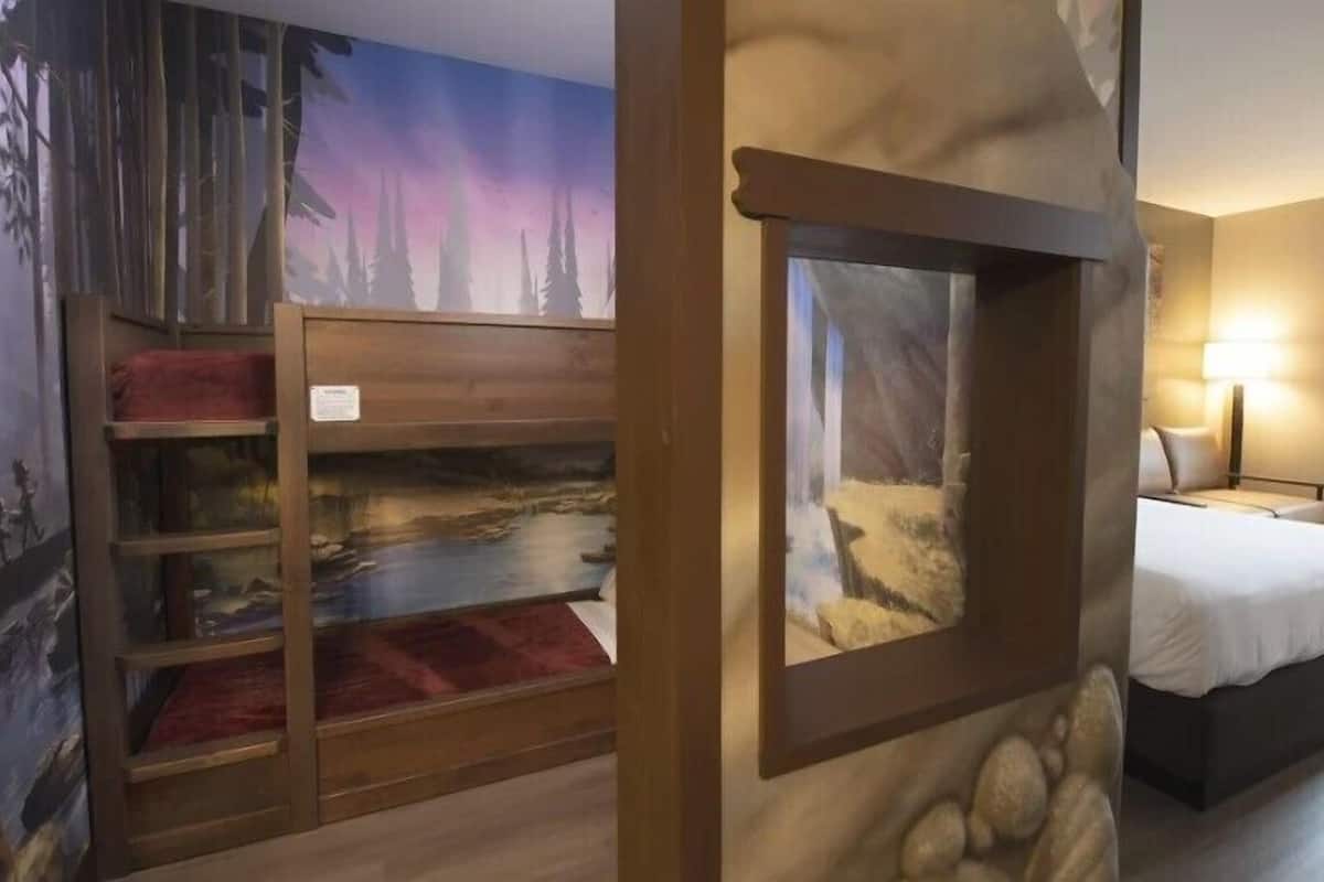A room with a bed, a window with a view of a forest, and a wall with a mural of a forest scene.