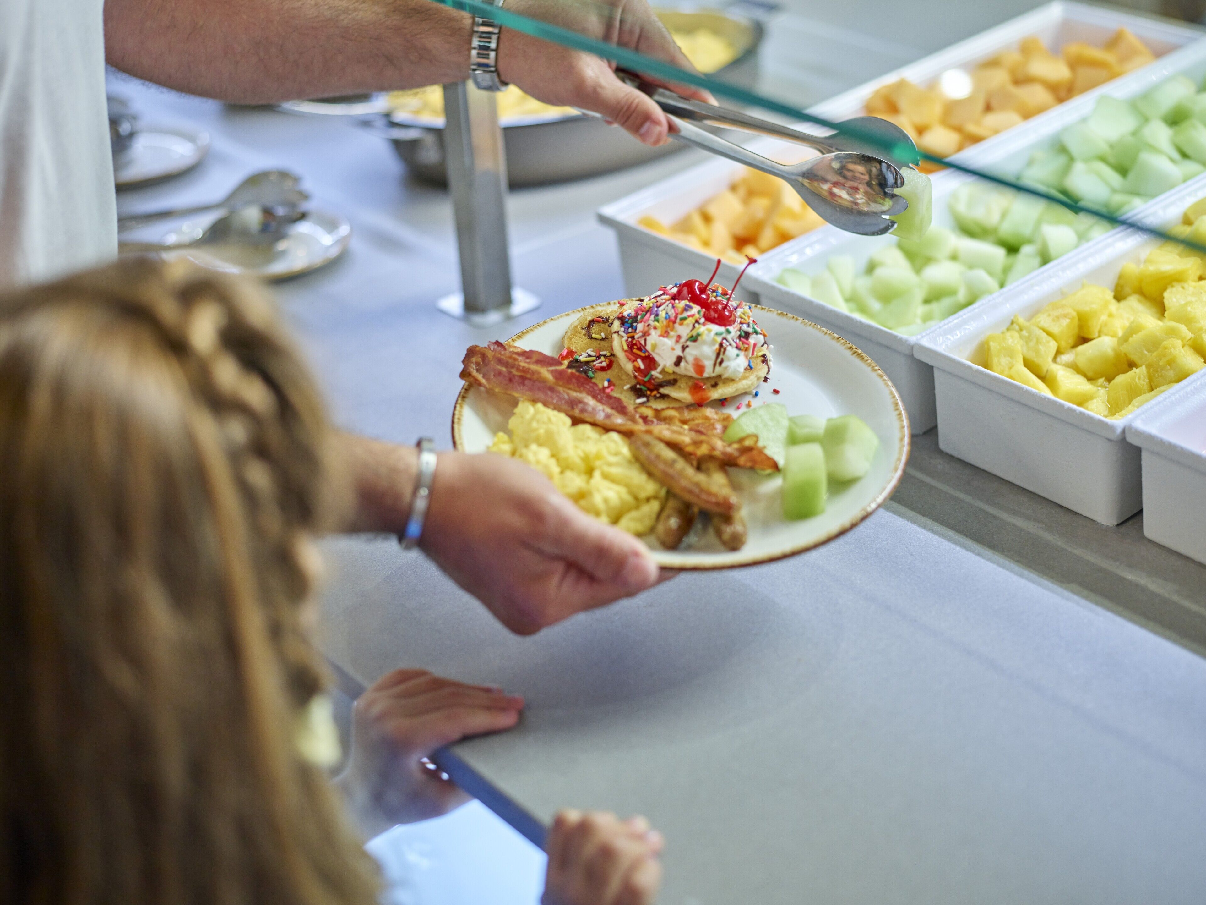 Een ontbijtbuffet met diverse gerechten, waaronder fruit en een schotel met spek en eieren.