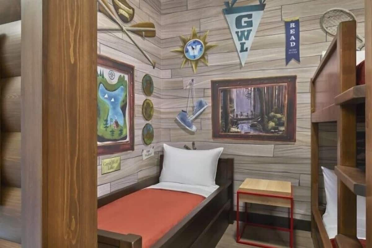 A room with a bed, a small table, and various wall decorations including a compass, a sun, and framed pictures.