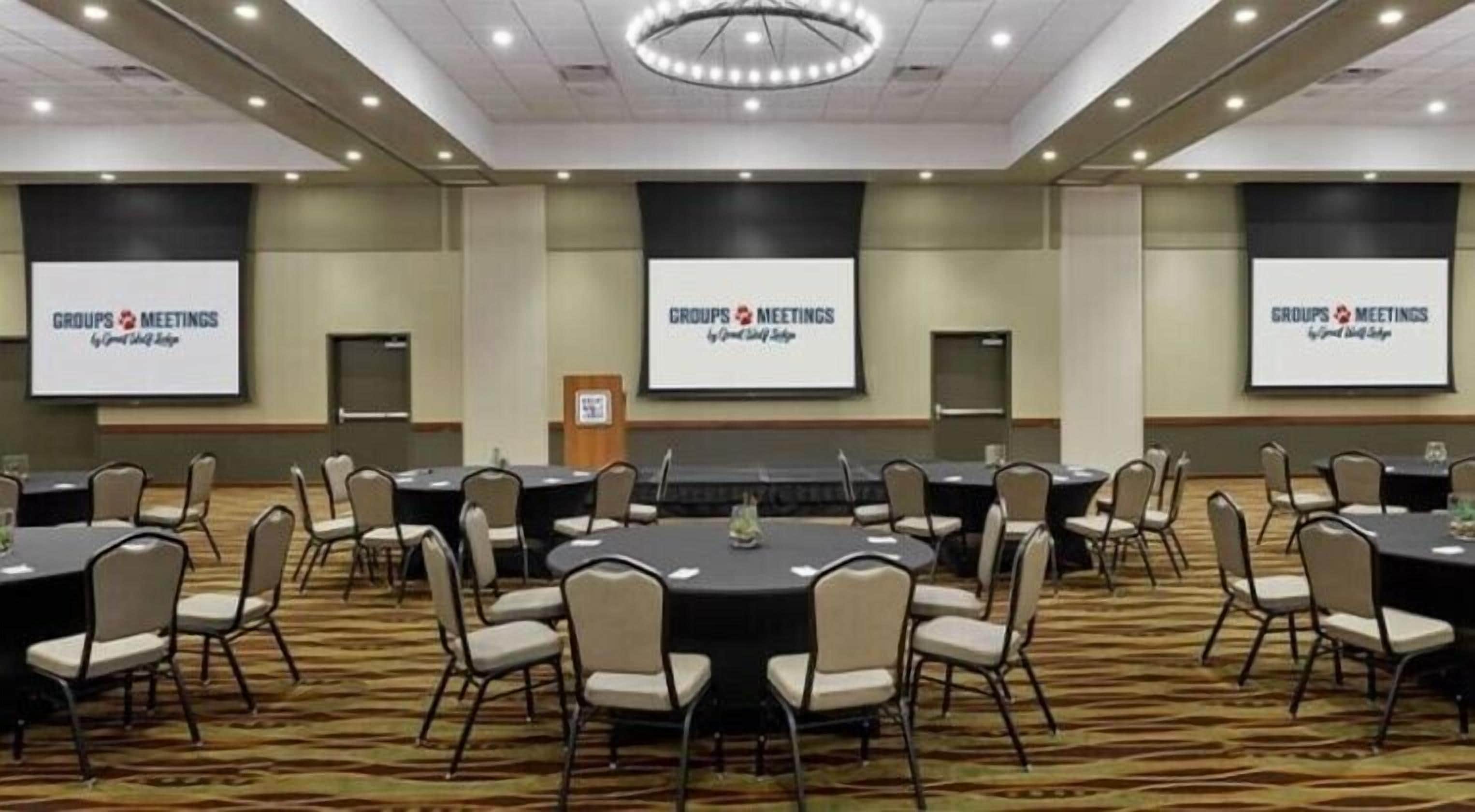 A conference room with multiple tables and chairs, equipped with screens displaying 'GROUPS MEETINGS' and 'Grand Sierra'.