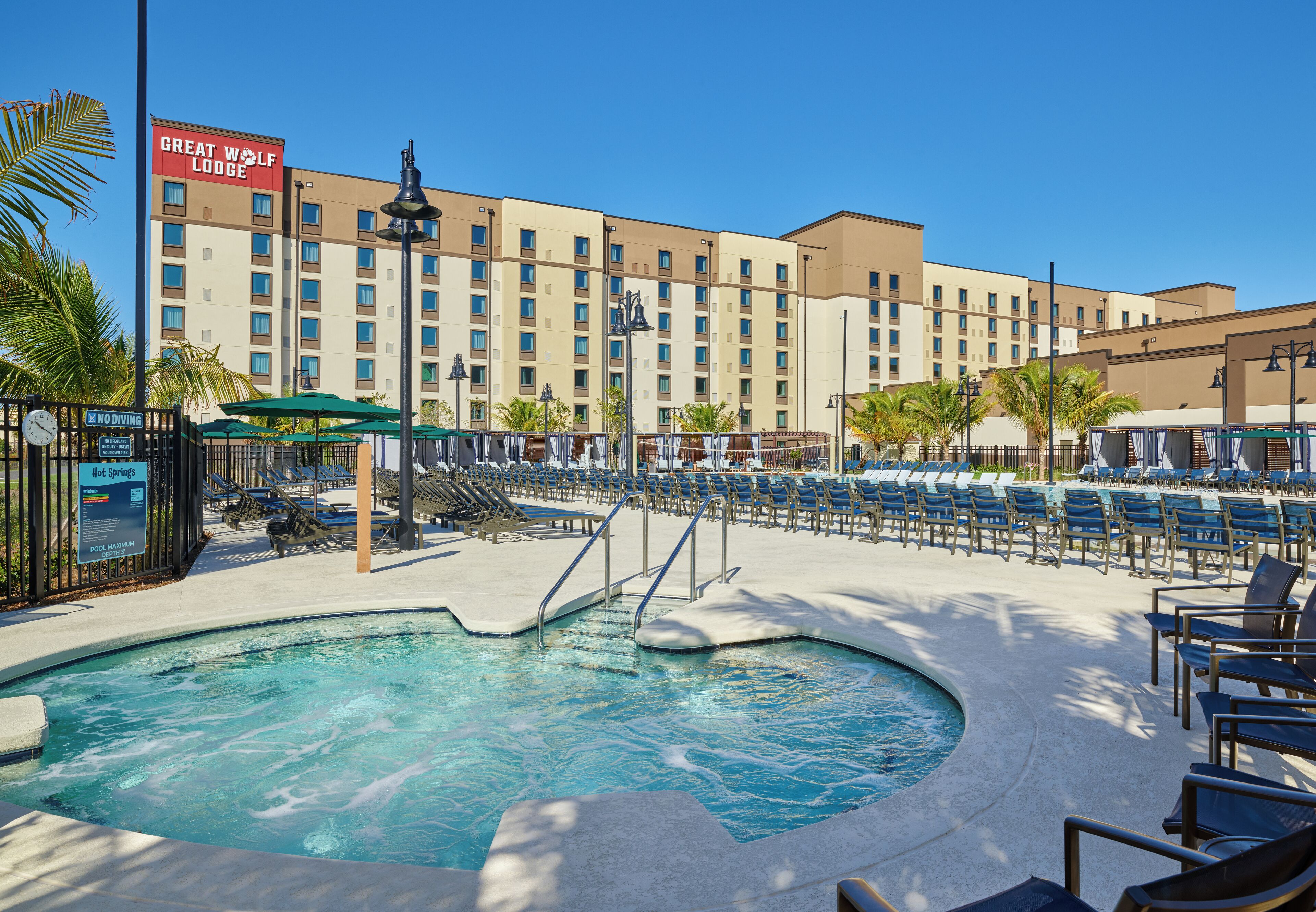 Zona de piscina de un hotel con sillas de descanso, un letrero de Great Wolf Lodge y un cartel de prohibición de clavados.