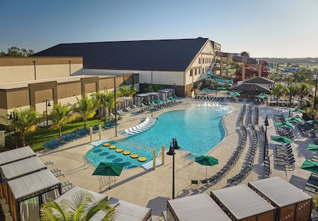 A resort pool area with a large pool, lounge chairs, umbrellas, and a water slide.