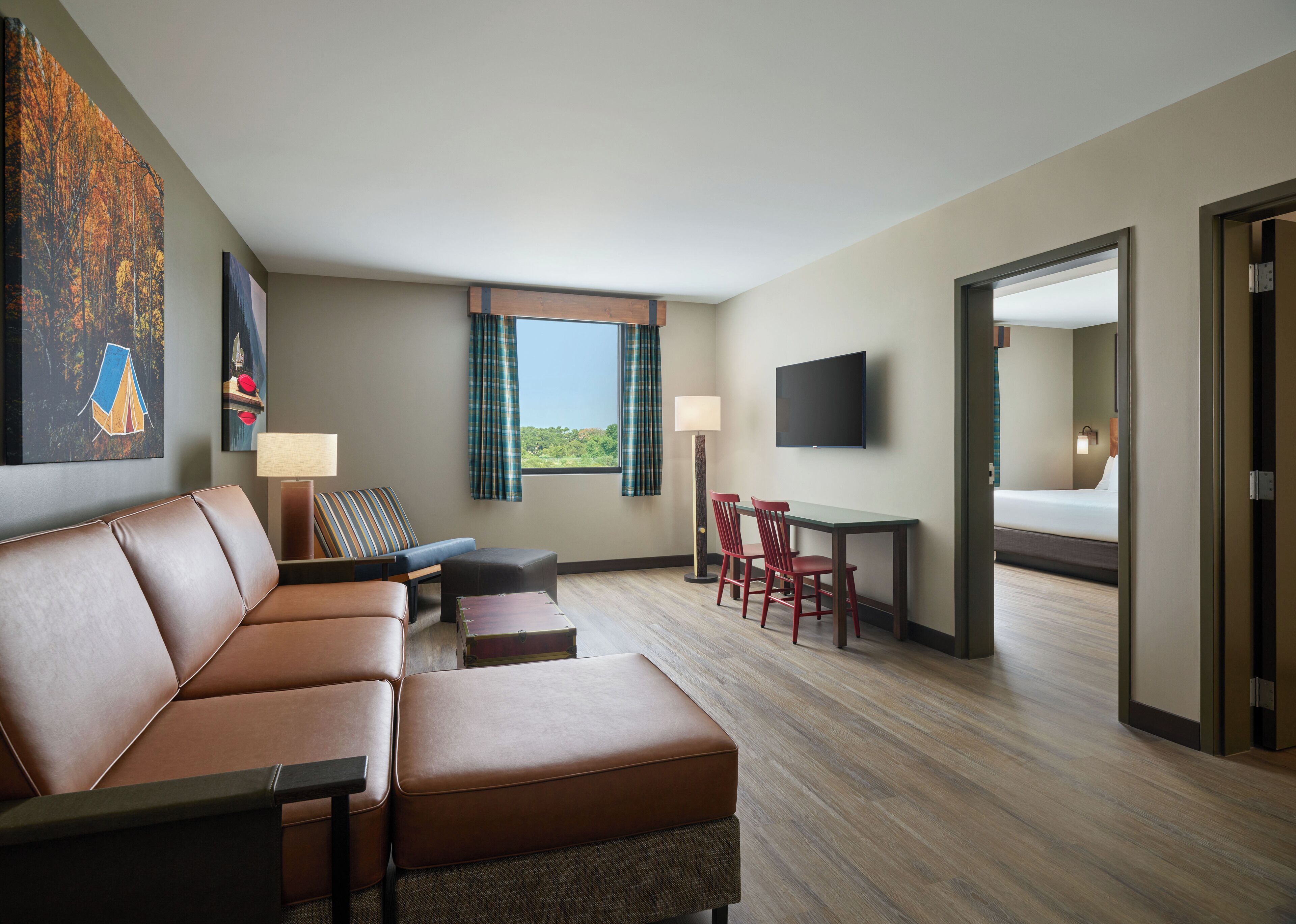 A hotel room with a sofa, a small table, two chairs, a TV, and a window with curtains.