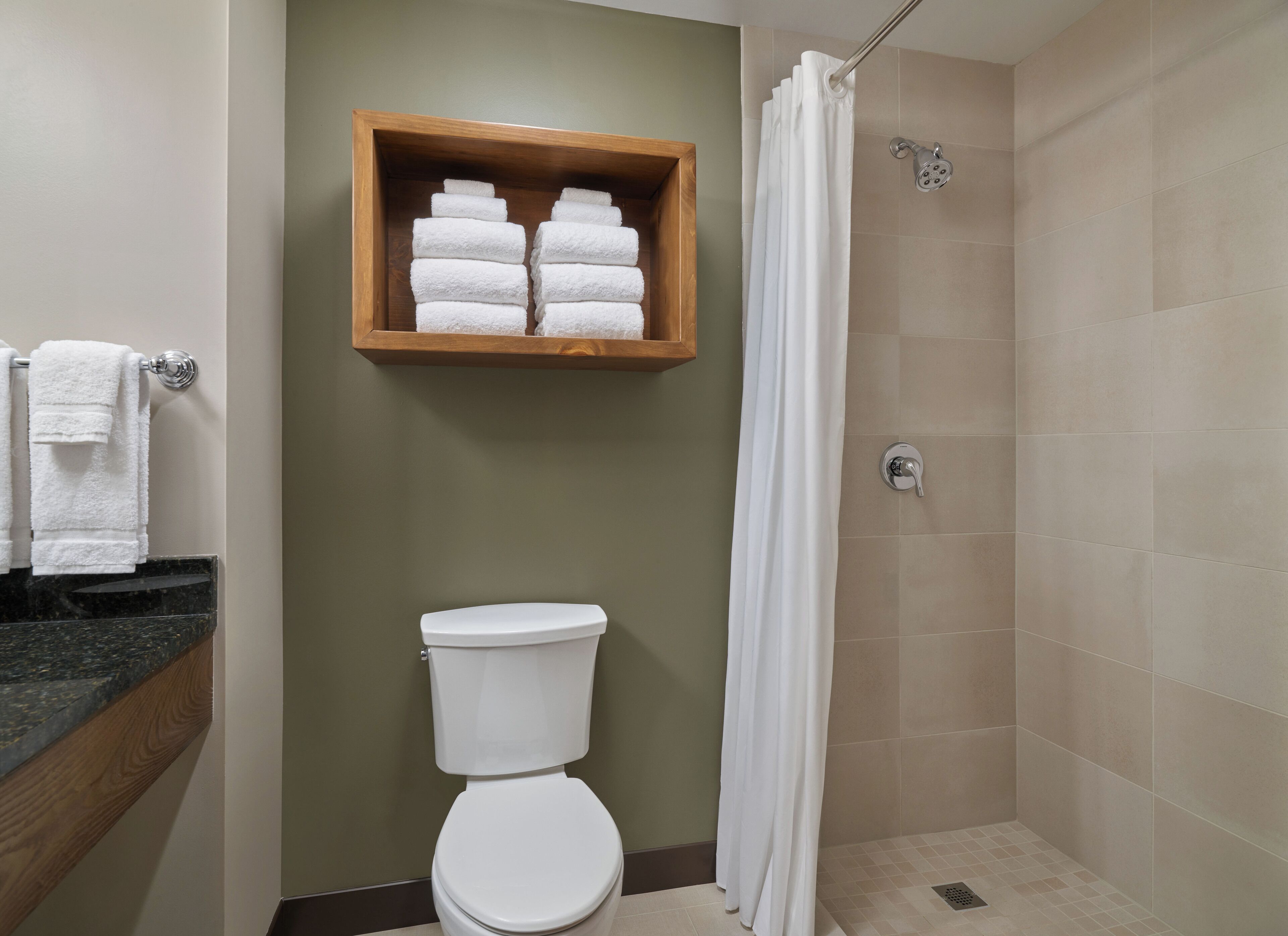 A bathroom with a toilet, a shower with a curtain, and a wooden shelf with towels.