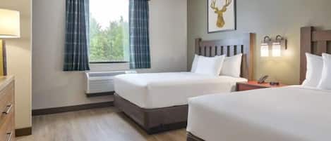 A hotel room with two beds, a window with curtains, a mounted deer head artwork, and a bedside table with a lamp.