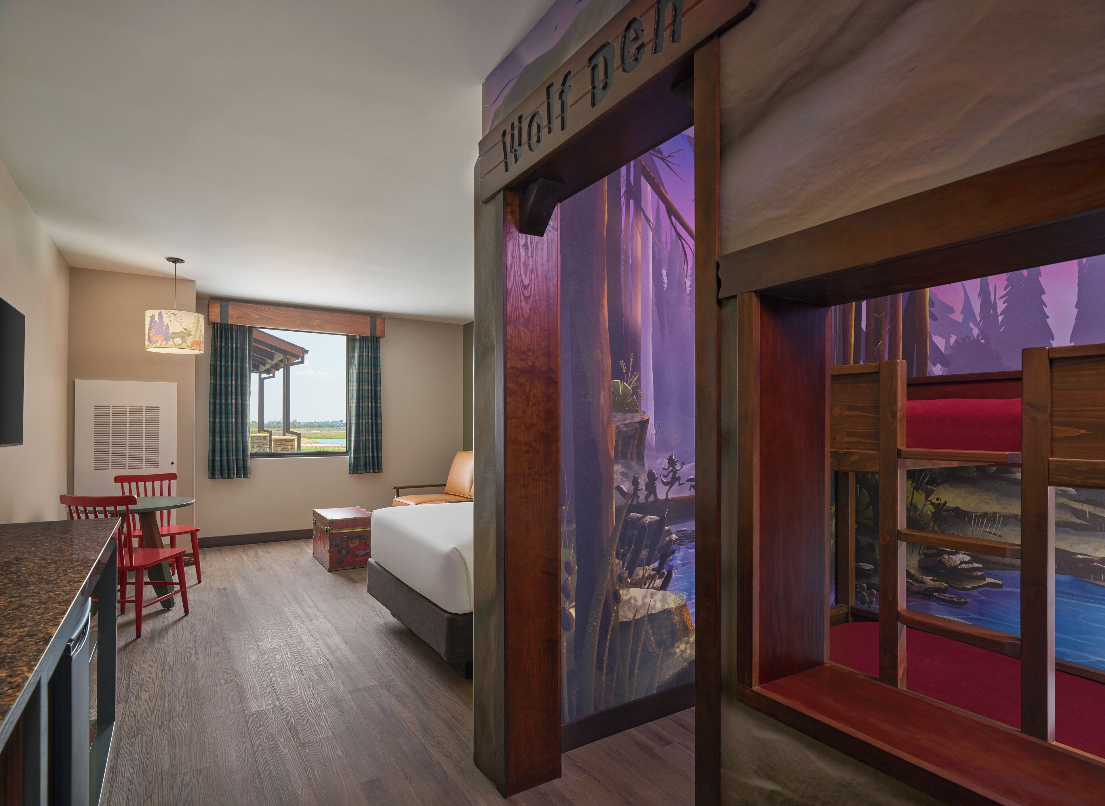 A hotel room with a bed, a desk, a chair, a window with curtains, and a mural depicting a forest scene.