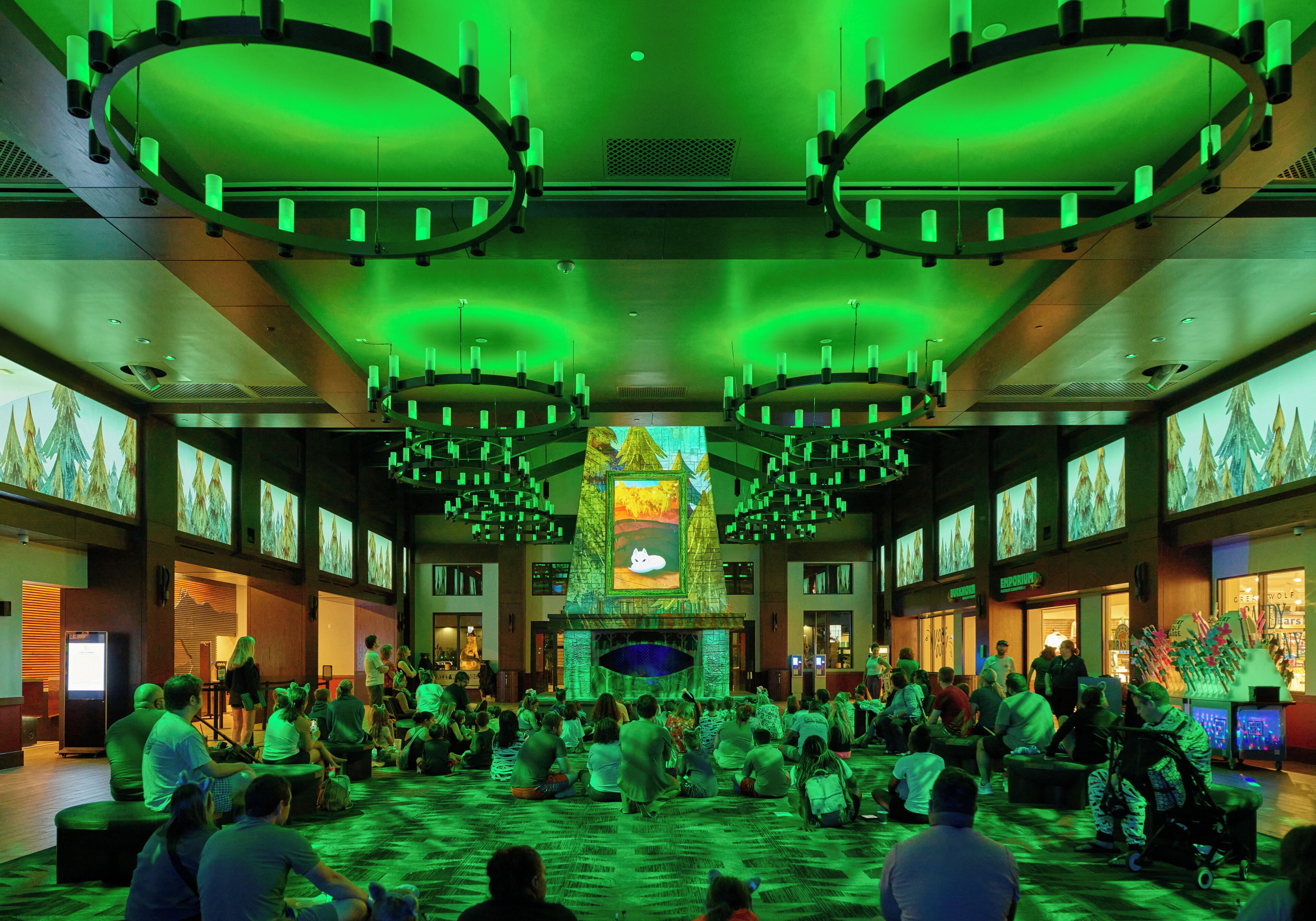 A spacious lobby with a high ceiling, multiple chandeliers, and a central fireplace.