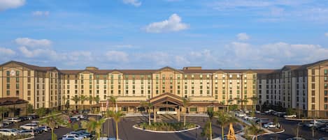 A hotel with a central entrance, multiple parking lots, and a clear sky.