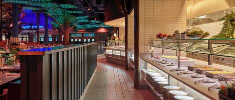 A buffet area with a variety of food items, a long counter with seating, and decorative ceiling lights.
