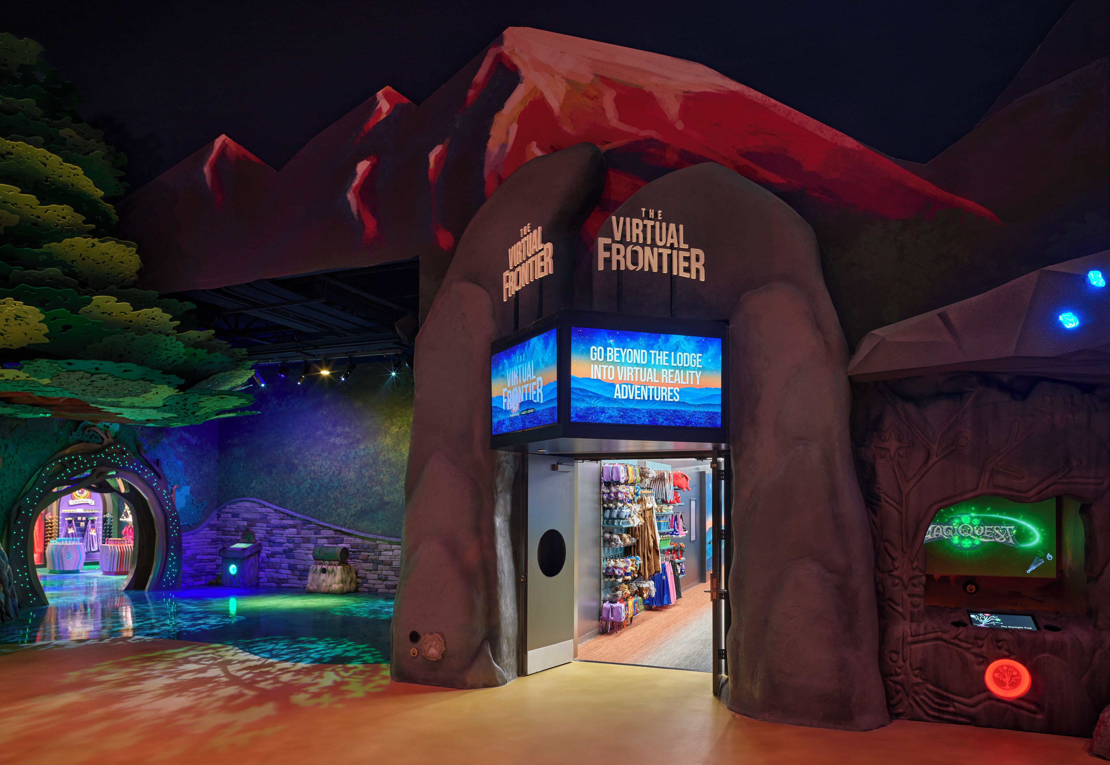 Entrada a una atracción en interiores con el letrero 'The Virtual Frontier', una tienda con el letrero 'Magic Questy', y un ambiente que recuerda a un bosque.